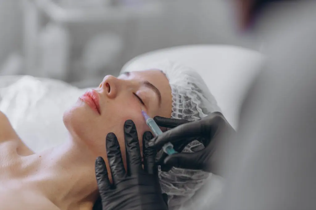A professional beautician in black gloves injects a young woman's face