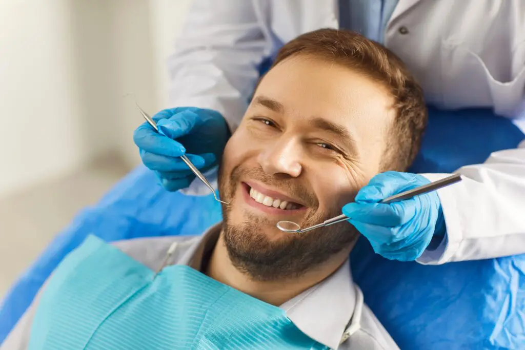 smiling man in a dental chair, dentist in blue gloves